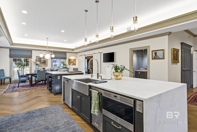 kitchen with a tray ceiling, pendant lighting, recessed lighting, stainless steel microwave, and an island with sink