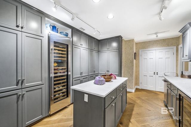 kitchen with wallpapered walls, wine cooler, ornamental molding, rail lighting, and gray cabinetry