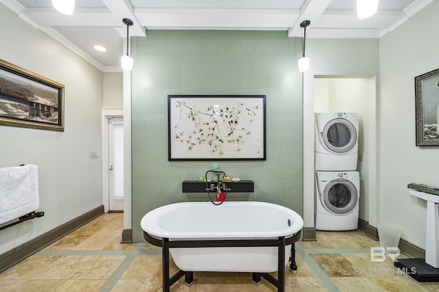 bathroom featuring a soaking tub, baseboards, beamed ceiling, and stacked washing maching and dryer