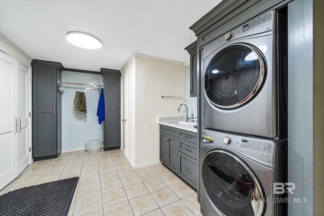 laundry area with light tile patterned floors, stacked washer / dryer, a sink, ornamental molding, and cabinet space