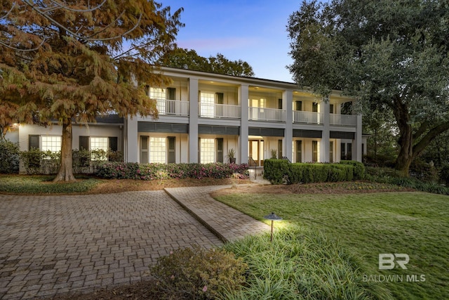 greek revival inspired property featuring a front lawn, a balcony, and stucco siding