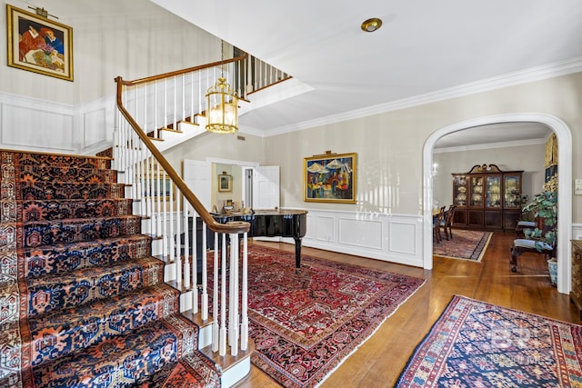 entryway featuring arched walkways, wainscoting, stairway, wood finished floors, and crown molding