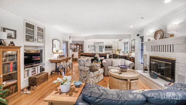 living room with crown molding, a fireplace, and light hardwood / wood-style flooring