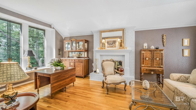 living room with crown molding, light wood-type flooring, a brick fireplace, lofted ceiling, and brick wall