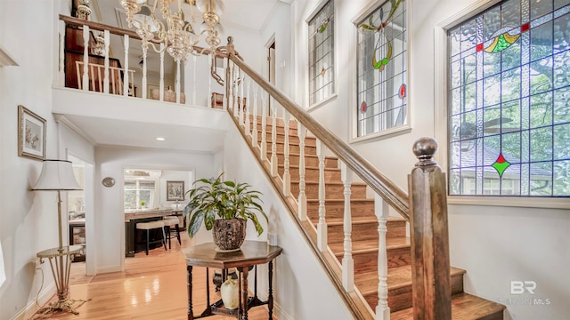 stairway featuring an inviting chandelier, a high ceiling, crown molding, and light hardwood / wood-style floors