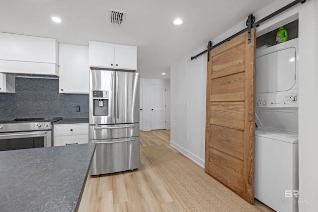 kitchen with appliances with stainless steel finishes, light hardwood / wood-style flooring, a barn door, stacked washer / drying machine, and white cabinets