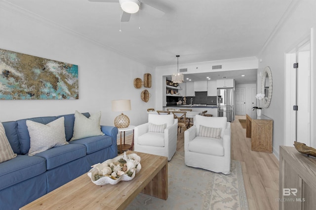 living room featuring light wood-type flooring, ornamental molding, and ceiling fan with notable chandelier