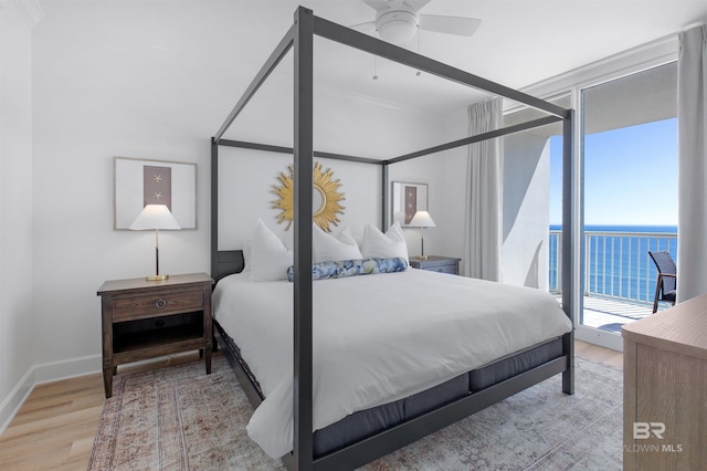 bedroom with a water view, light hardwood / wood-style flooring, expansive windows, and access to outside