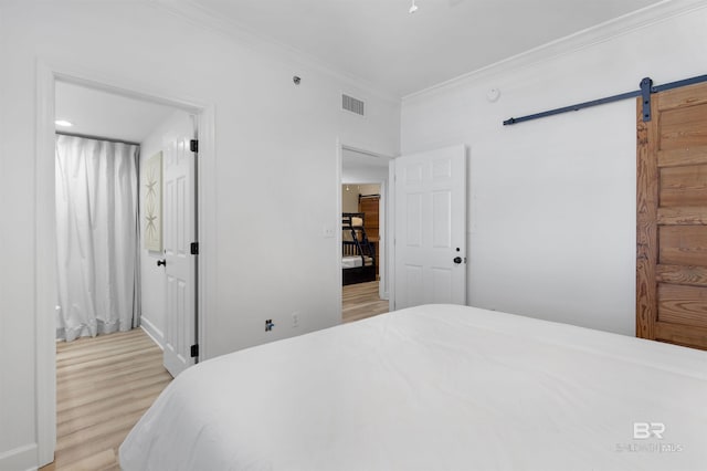 bedroom featuring ornamental molding, light hardwood / wood-style flooring, and a barn door