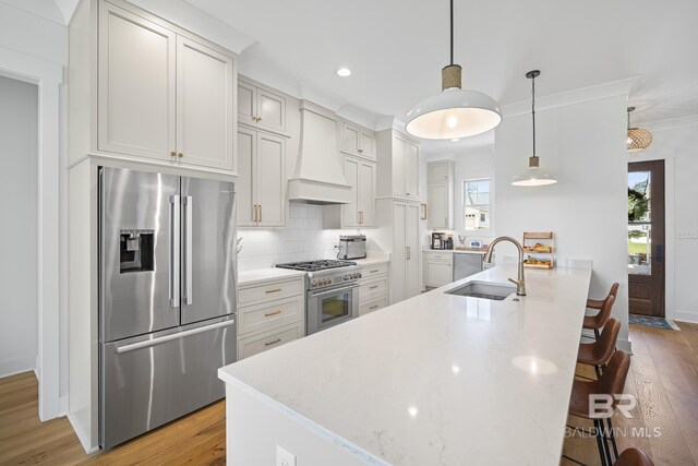 313 Cuban Lily Dr, Fairhope, AL 36532 - kitchen featuring premium appliances, custom exhaust hood, a sink, light wood-type flooring, and a kitchen bar