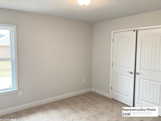 unfurnished bedroom with multiple windows, a closet, a textured ceiling, and light colored carpet