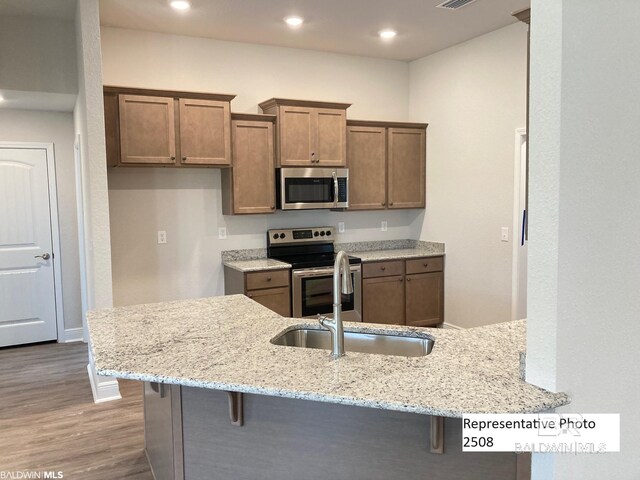 kitchen featuring kitchen peninsula, appliances with stainless steel finishes, light stone countertops, and a breakfast bar