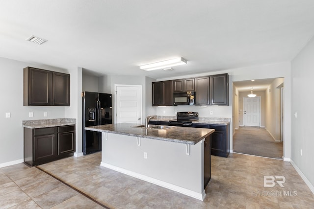 kitchen featuring black appliances, a kitchen island with sink, sink, and a breakfast bar