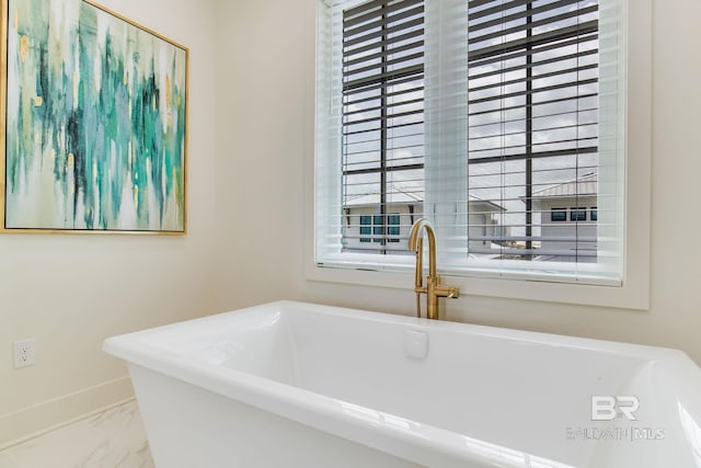 bathroom with marble finish floor, baseboards, and a freestanding tub