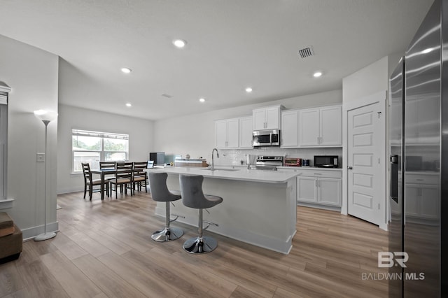 kitchen with a sink, white cabinets, stainless steel appliances, and light wood-type flooring