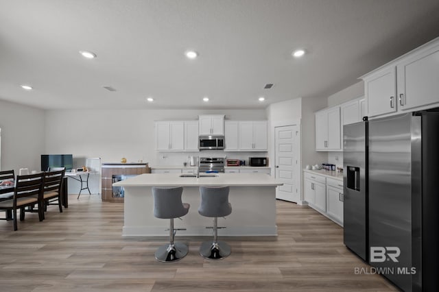 kitchen with recessed lighting, a kitchen island with sink, appliances with stainless steel finishes, light countertops, and white cabinetry