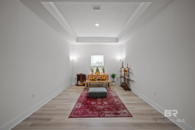 sitting room with visible vents, light wood-type flooring, crown molding, and a tray ceiling