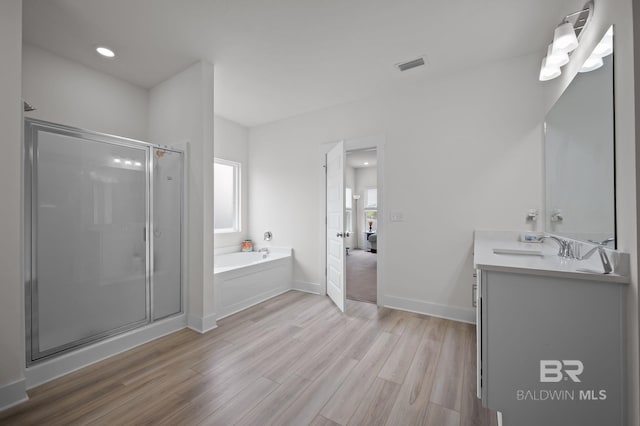 ensuite bathroom featuring a shower stall, vanity, visible vents, a garden tub, and wood finished floors