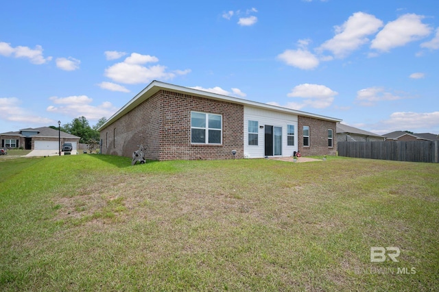 rear view of house with a lawn, fence, and brick siding