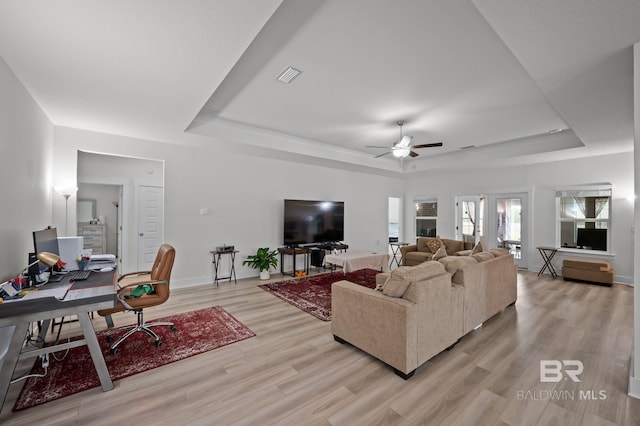 living area with visible vents, ceiling fan, light wood finished floors, and a tray ceiling