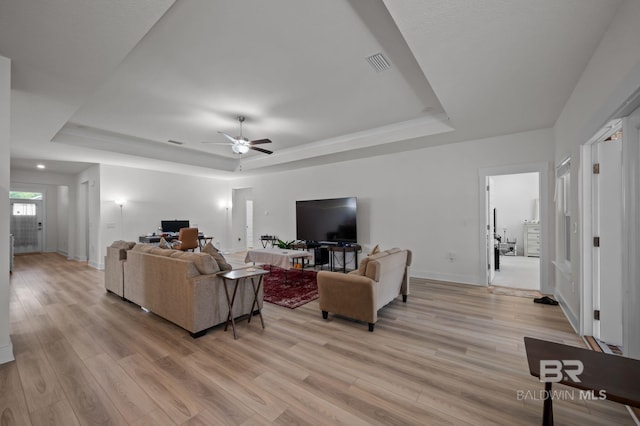 living room featuring a ceiling fan, visible vents, light wood-style floors, and a tray ceiling