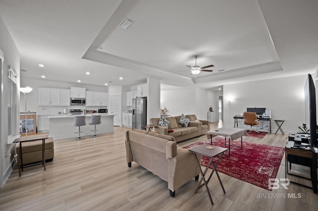 living room featuring visible vents, a raised ceiling, a ceiling fan, and light wood-style floors