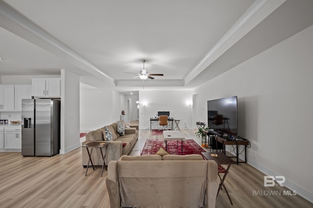 living room featuring baseboards, a raised ceiling, ceiling fan, and light wood-style floors