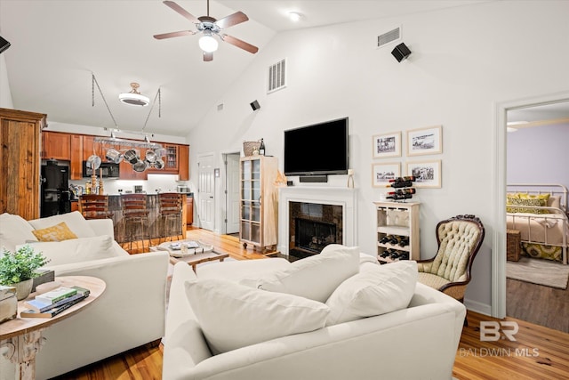 living area with high vaulted ceiling, a fireplace, a ceiling fan, visible vents, and light wood-style floors