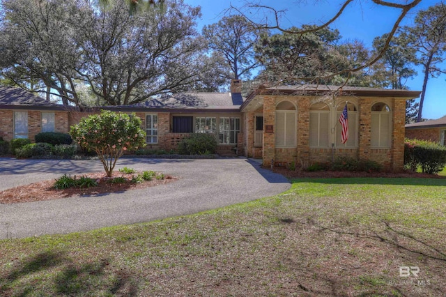 view of front facade with aphalt driveway, brick siding, a front yard, and a chimney