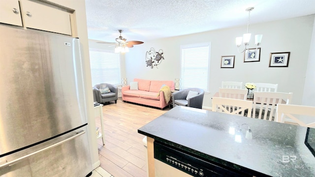 kitchen with ceiling fan with notable chandelier, a textured ceiling, light hardwood / wood-style floors, hanging light fixtures, and stainless steel refrigerator