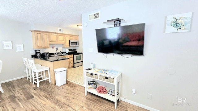 kitchen featuring a textured ceiling, light brown cabinets, stainless steel appliances, sink, and a breakfast bar