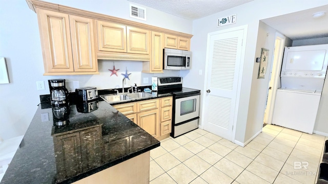 kitchen with stacked washer and dryer, stainless steel appliances, light brown cabinetry, dark stone countertops, and sink