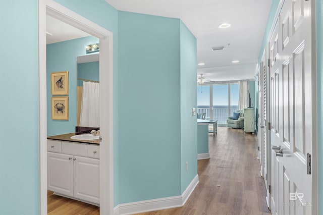 hall with recessed lighting, visible vents, a sink, light wood-type flooring, and baseboards