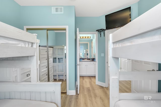 bedroom with light wood-type flooring, baseboards, visible vents, and a closet