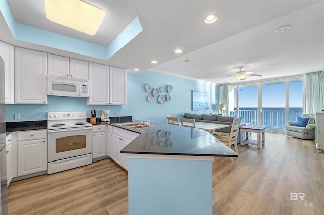 kitchen with white appliances, light wood finished floors, dark countertops, open floor plan, and a peninsula