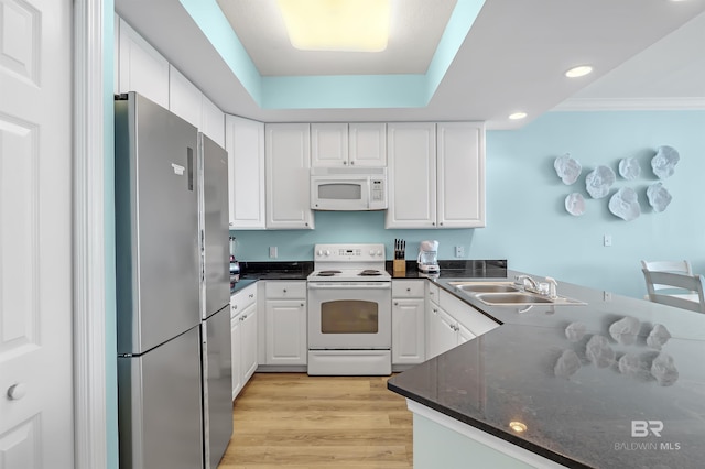 kitchen featuring a raised ceiling, white cabinetry, a sink, light wood-type flooring, and white appliances