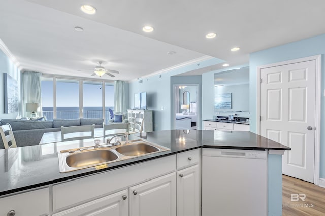 kitchen with dark countertops, white dishwasher, white cabinetry, and a sink