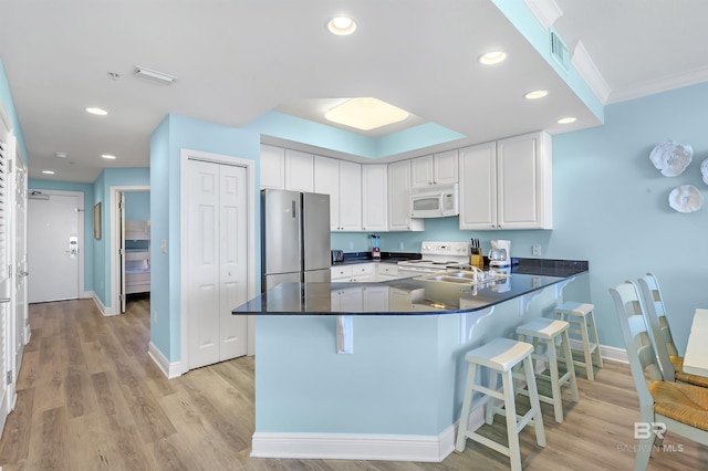 kitchen featuring recessed lighting, a peninsula, white appliances, white cabinetry, and dark countertops