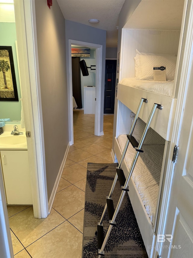 hallway with baseboards, light tile patterned flooring, and a sink