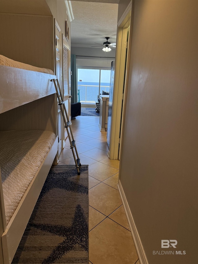 hall featuring baseboards, light tile patterned flooring, crown molding, and a textured ceiling