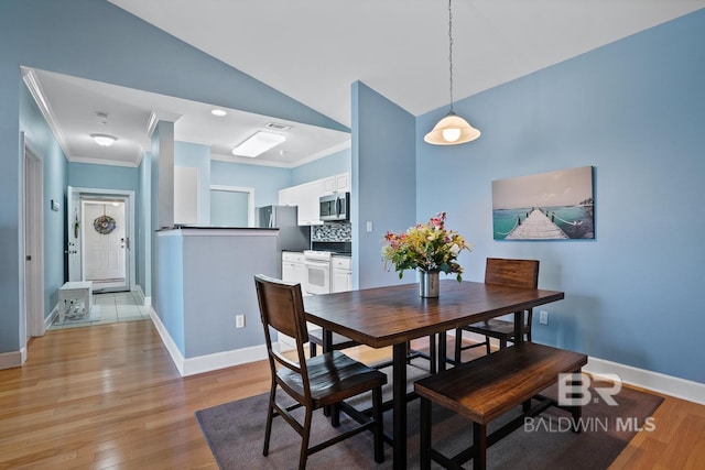 dining space with light wood finished floors, lofted ceiling, visible vents, ornamental molding, and baseboards