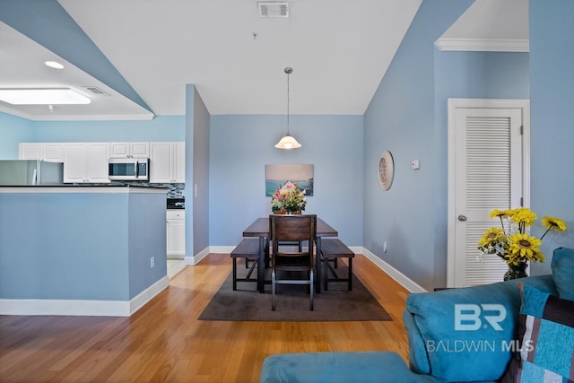 dining room featuring crown molding, light wood-type flooring, visible vents, and baseboards