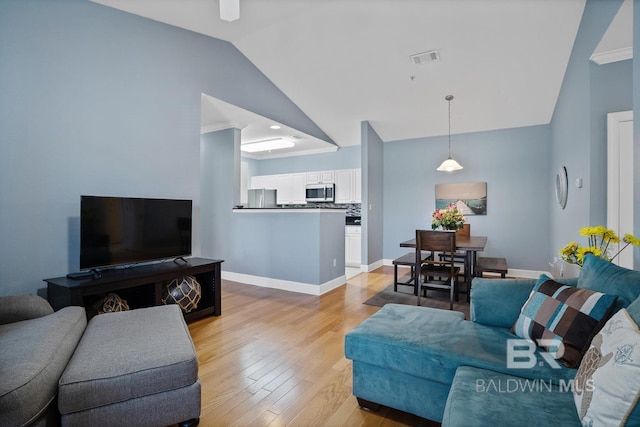 living area with baseboards, vaulted ceiling, visible vents, and light wood-style floors