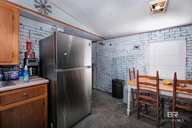 kitchen with brick wall, stainless steel refrigerator, vaulted ceiling, and a textured ceiling