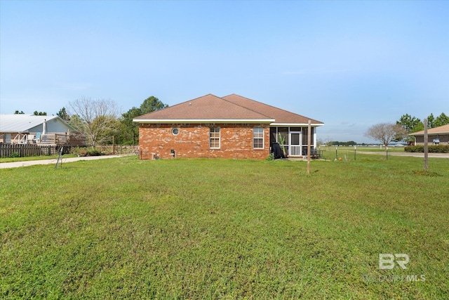 back of property with brick siding, a sunroom, fence, and a yard