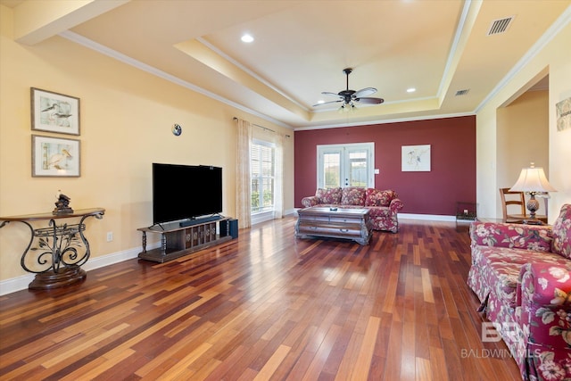 living room featuring hardwood / wood-style floors, a tray ceiling, visible vents, and a ceiling fan