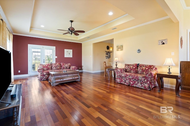 living room with a tray ceiling, crown molding, baseboards, hardwood / wood-style flooring, and a ceiling fan