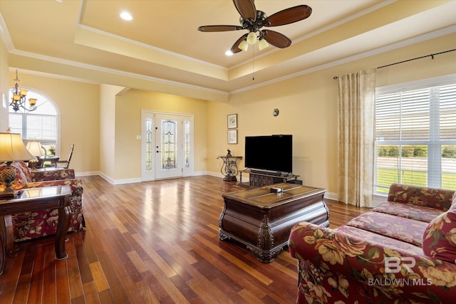 living room featuring a tray ceiling, ceiling fan with notable chandelier, wood finished floors, and ornamental molding