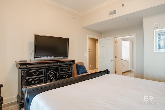 bedroom with wood finished floors, baseboards, visible vents, ornamental molding, and connected bathroom