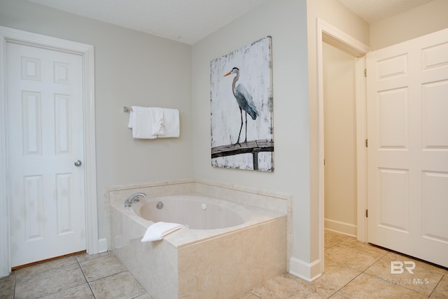 full bath featuring tile patterned flooring, a textured ceiling, a bath, and baseboards